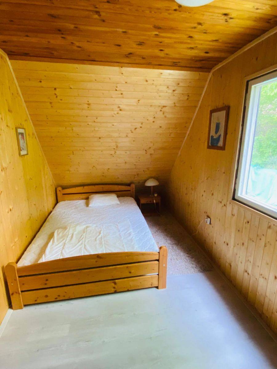 Ložnice obložená dřevem s postelí pod šikmým stropem